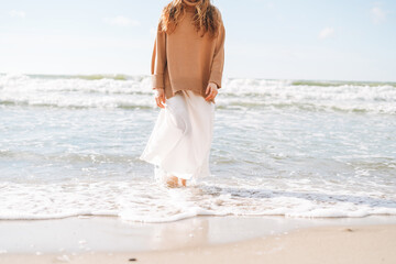 Fototapeta na wymiar Crop photo of Young beautiful woman in beige sweater enjoying life on sea beach on sunset