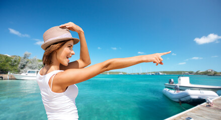 travel, tourism and summer vacation concept - happy smiling woman in hat pointing at something over...