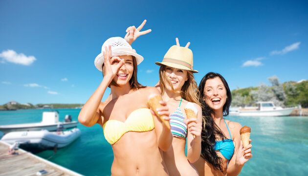 travel, tourism and summer vacation concept - happy women in bikinis with ice cream over wooden pier and boat on tropical beach background in french polynesia