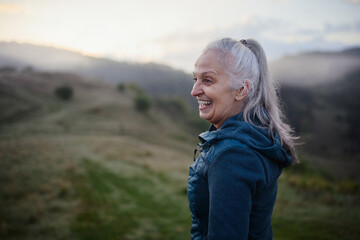 Senior woman hiking in nature on early morning with fog and mountains in background.