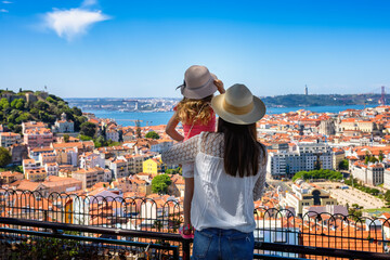 A tourist mother and her little daughter enjoy the view of the beautiful cityscape of Lisbon, with the colorful houses and roofs, Portugal - obrazy, fototapety, plakaty