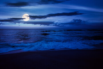 calm sea scenery at night. waves wash empty sandy beach in full moon light. relax and summer vacation concept. warm velvet season weather with clouds on the sky