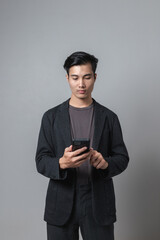 Raised waist of a smiling Asian handsome man in a semi-formal suit using a cell phone in a separate gray studio background.