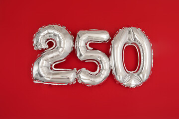 From above of silver shiny balloons demonstrating number 250 two hundred and fifty on red background with scattered glitter - obrazy, fototapety, plakaty