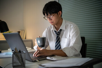 Alone Working Late at Night.Asian business man at workplace in office holding his head on hands...