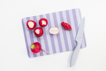Fresh organic ripe red radish cut in pieces on cutting board with knife on white background. Vegetarian, vegan, raw spring food. Close-up, copy space