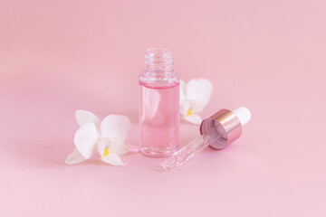 Obraz na płótnie Canvas Dropper glass bottle near white orchid flowers on light pink, Mockup. Skincare product
