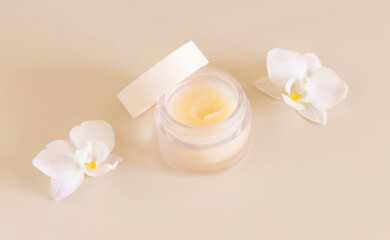 Fototapeta na wymiar Cosmetic glass jar near white orchid flowers on light yellow close up