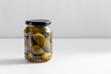food, storage and preserve concept - close up of jar with pickled cucumbers on white table