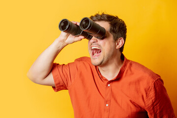Guy in orange shirt watch in binoculars on yellow background