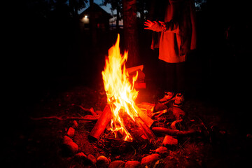 Girl tourist, warming herself by the fire at night in a tourist camp. The concept of an active lifestyle.