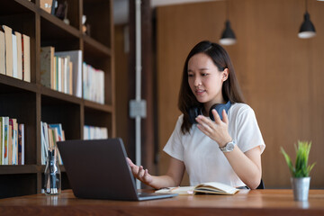 Asian woman online tutor remote teacher wearing glasses speaking to webcam chat explaining online class video call school lesson looking at laptop virtual conference meeting work at home office.