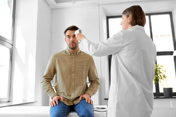 medicine, healthcare and people concept - female doctor with infrared forehead thermometer...
