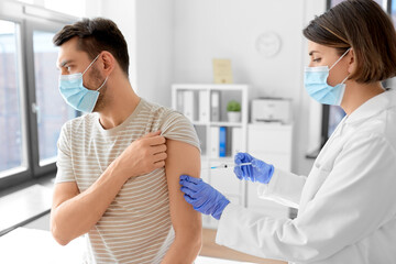 Obraz premium health, medicine and pandemic concept - female doctor or nurse wearing protective medical mask and gloves with syringe vaccinating male patient at hospital