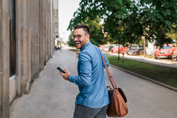 Cheerful entrepreneur looking over shoulder while walking on sidewalk in the city