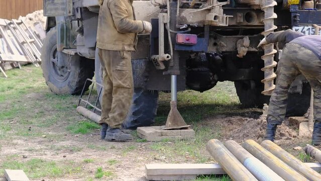 Team of workers with drilling rig on car are drilling artesian well for water in ground. Insertion of metal casing pipe into ground, installation of individual drinking supply, June 28, 2022, Russia, 