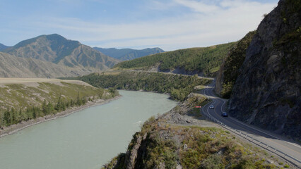 Traffic cars on Chuya highway road between mountains and Katun river under blue sky in Altai