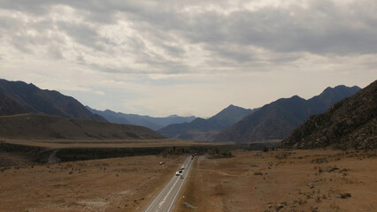 Mountains valley of Altai with traffic cars on Chuya highway under dramatic sky