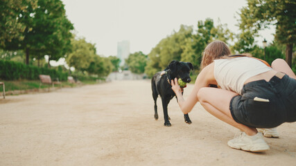 Girl walks along the path in the park with back dog.