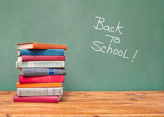 stack of books on the table against the background of the school blackboard with the inscription back to school