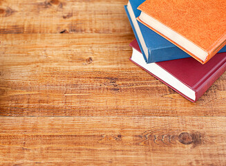 three multi-colored books lie on a wooden table. View from above