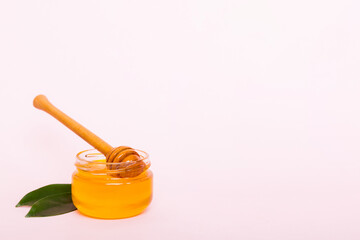 Honey in jar with leaves and honey dipper on colored background top view with copy text