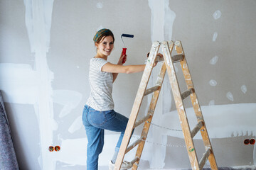 Young woman renovating her apartment and standing on wooden ladder