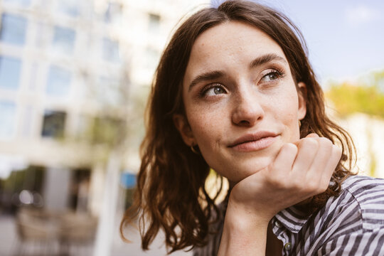 pensive young woman sitting in city looking to the side