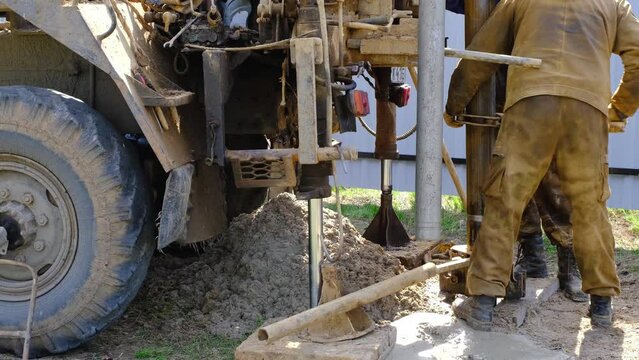 Team of workers with drilling rig on car are drilling artesian well for water in ground. Insertion of metal casing pipe into ground, installation of individual drinking supply, June 28, 2022, Russia, 