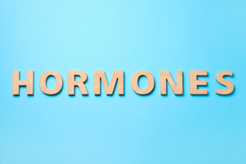 Word Hormones made of wooden letters on light blue background, flat lay