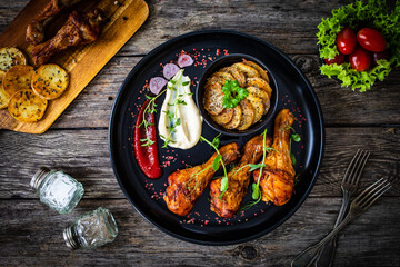 Barbecued chicken drumsticks with fried potato on wooden table
