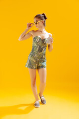 Full-length portrait of beautiful young girl posing isolated over yellow studio background