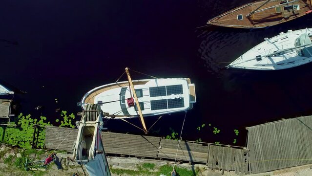 Top drone shot of large white crane preparing to unload a newly prepared white motor boat slong the shoreline at daytime. 