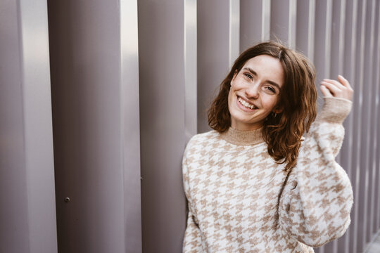 Young smiling woman stands in front of modern steel wall and looks to the camera laughing