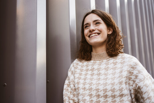 Young smiling woman stands in front of modern steel wall and looks to the side laughing