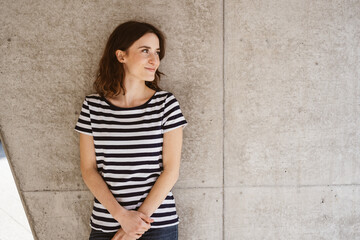 Young serious woman stands in front of modern brown wall and looks to the side