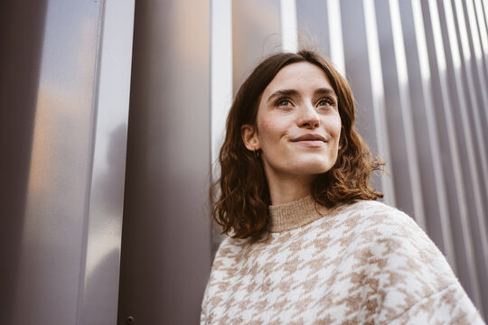 Young smiling woman stands in front of modern steel wall and looks up