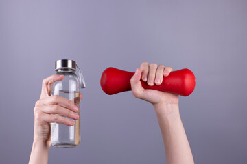 Girl 's hand holding red dumbbell and bottle of water on grey background. concept.  Sport and healthy lifestyle concept with Copy space.