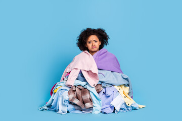 Fototapeta premium Photo of stressed depressed young woman covered big stack clothes isolated blue color background