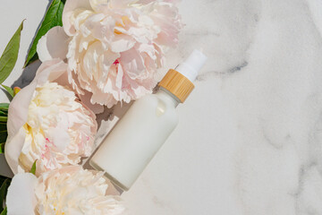 Close-up of a white bottle with natural cosmetic cream and blooming pink peony flowers on a white marble background. Cosmetic beauty concept. Copy space