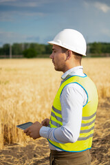 Fototapeta premium an engineer with a tablet in his hands stands in the middle of a green field, an agronomist in a field with wheat checks the harvest, summer day, smart farm, farming activities, eco products.