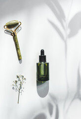 Beauty setting with green cosmetic bottle and jade massage roller at white background with floral...