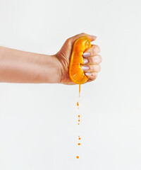 Woman hand squeezing halves of orange at white background with juice dripping. Front view.