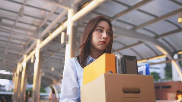 Portrait of young Asian woman walking and holding box of items after being laid off from job due to recession and economic stress in industry