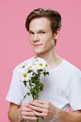close-up portrait of a happy guy with large, white daisies in his hands on a pink background with space for text