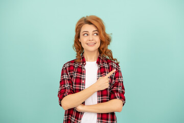 glad redhead woman in checkered shirt pointing finger on blue background