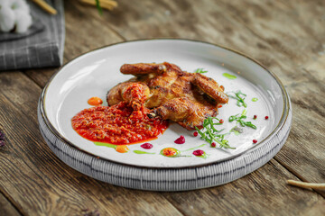 Portion of roasted tobacco quail with pepper sauce on wooden background