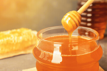 Sweet honey dripping from dipper into glass jar, closeup