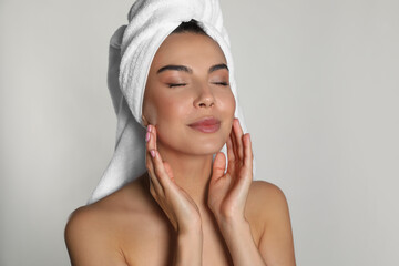 Beautiful young woman with towel on head against light background