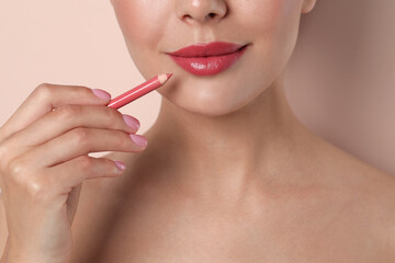 Young woman with beautiful pink lip pencil on light background, closeup